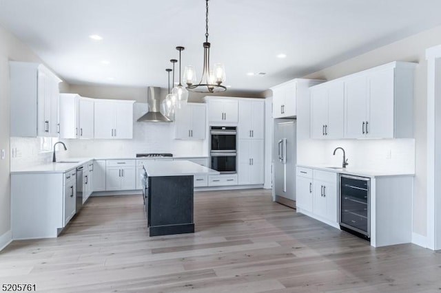 kitchen with beverage cooler, stainless steel appliances, a kitchen island, a sink, and wall chimney exhaust hood