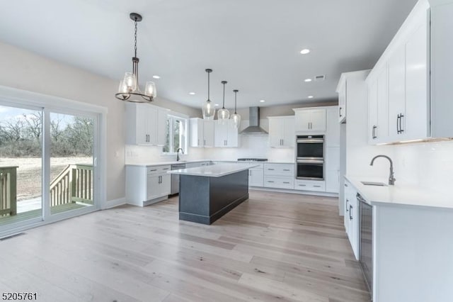 kitchen featuring wall chimney exhaust hood, a sink, light wood-style flooring, and a center island