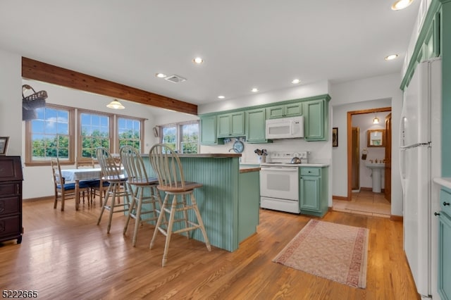 kitchen with light hardwood / wood-style flooring, white appliances, a kitchen breakfast bar, and green cabinets