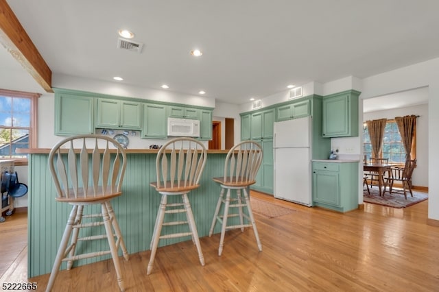 kitchen featuring green cabinets, light hardwood / wood-style floors, white appliances, and a breakfast bar