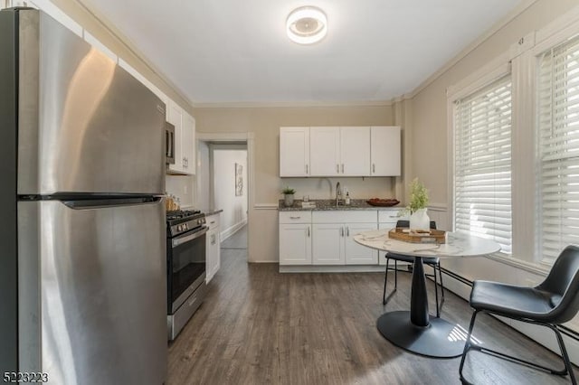 kitchen featuring dark wood-style flooring, appliances with stainless steel finishes, white cabinets, stone countertops, and a sink