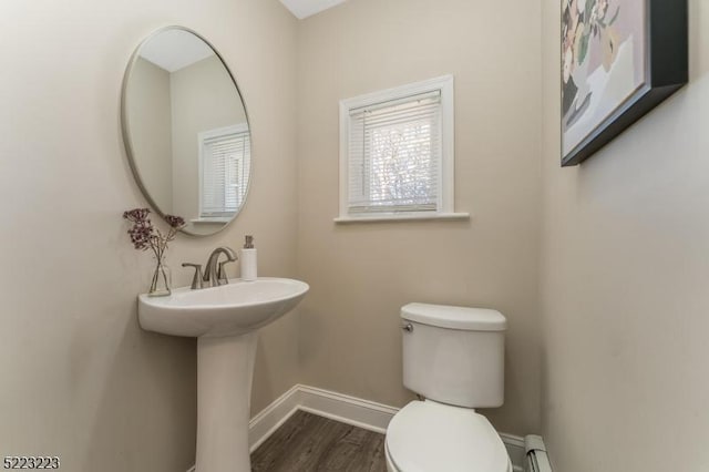 half bath featuring baseboard heating, toilet, baseboards, and wood finished floors