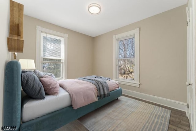 bedroom with multiple windows, wood finished floors, and baseboards