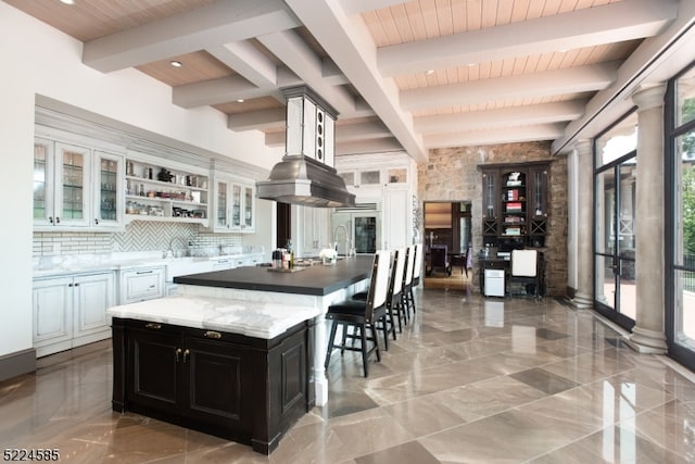 kitchen with beam ceiling, an island with sink, backsplash, and white cabinets