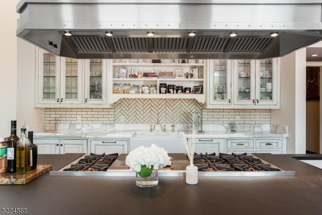 kitchen featuring light stone countertops, white cabinetry, backsplash, and fume extractor