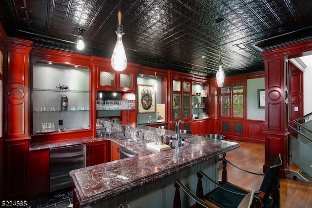 bar featuring stainless steel dishwasher, beverage cooler, dark wood-type flooring, hanging light fixtures, and dark stone countertops