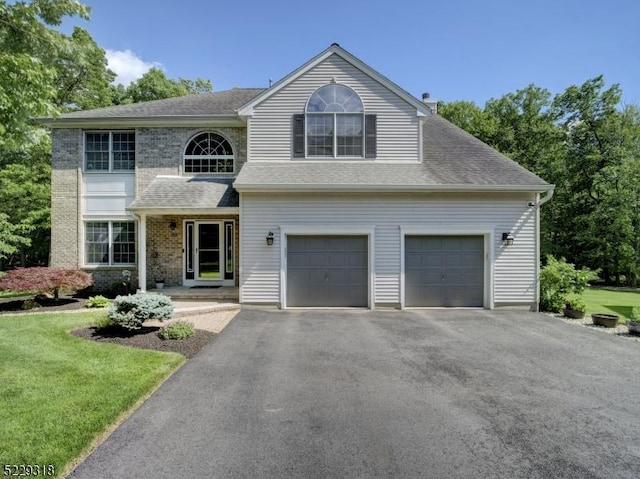 traditional home with aphalt driveway, roof with shingles, a front yard, a garage, and brick siding