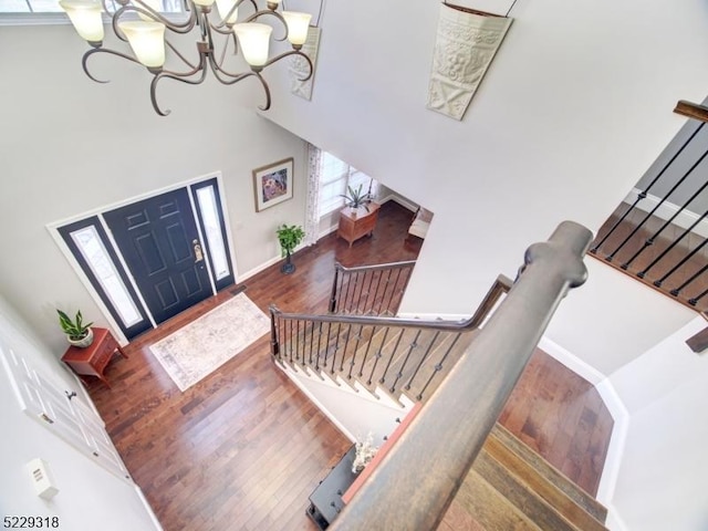 entryway with baseboards, stairway, a towering ceiling, wood finished floors, and a notable chandelier