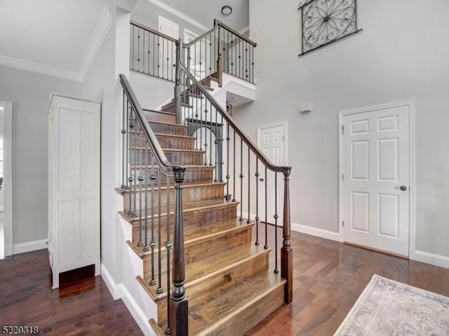 staircase with crown molding, a high ceiling, wood finished floors, and baseboards