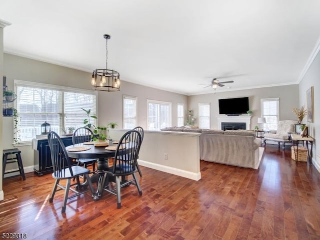 dining area with ornamental molding, ceiling fan with notable chandelier, dark wood-style flooring, and baseboards