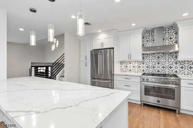 kitchen with tasteful backsplash, stainless steel appliances, wall chimney range hood, pendant lighting, and white cabinets