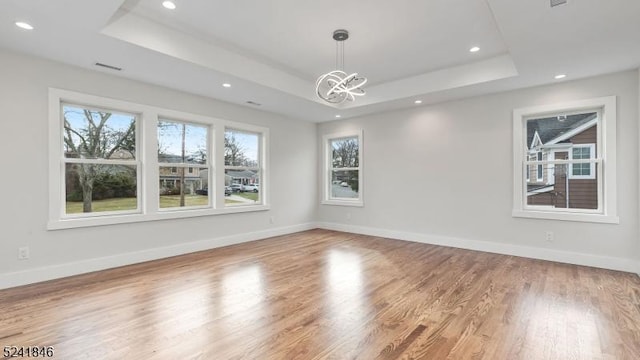 empty room featuring hardwood / wood-style floors, a raised ceiling, and a notable chandelier