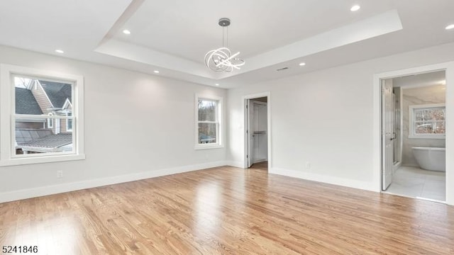 unfurnished bedroom with ensuite bathroom, a raised ceiling, a walk in closet, light wood-type flooring, and multiple windows