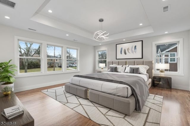 bedroom with a raised ceiling, light hardwood / wood-style flooring, and a notable chandelier