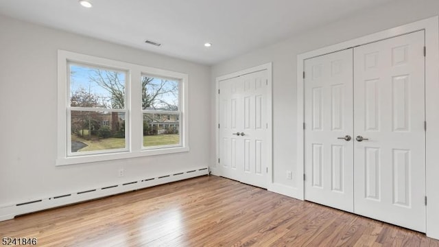 unfurnished bedroom featuring light wood-type flooring, baseboard heating, and multiple closets