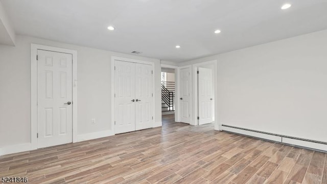 unfurnished bedroom with light hardwood / wood-style floors, two closets, and a baseboard heating unit