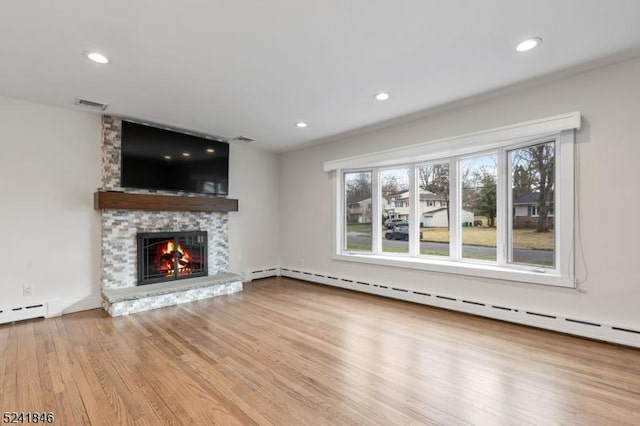 unfurnished living room featuring light hardwood / wood-style floors, baseboard heating, a fireplace, and a wealth of natural light