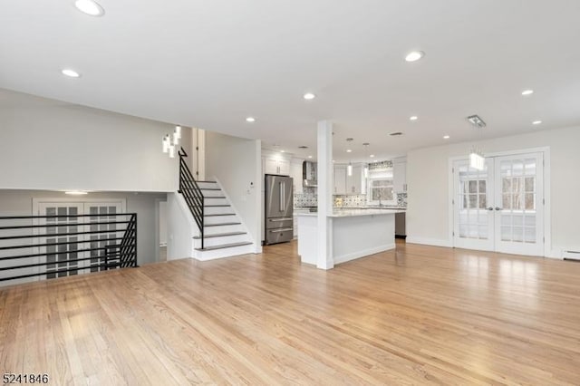 unfurnished living room with light hardwood / wood-style floors, baseboard heating, and french doors