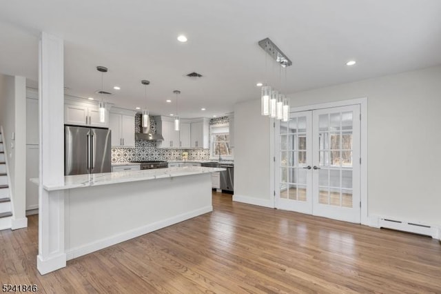 kitchen with appliances with stainless steel finishes, french doors, wall chimney exhaust hood, white cabinets, and hanging light fixtures