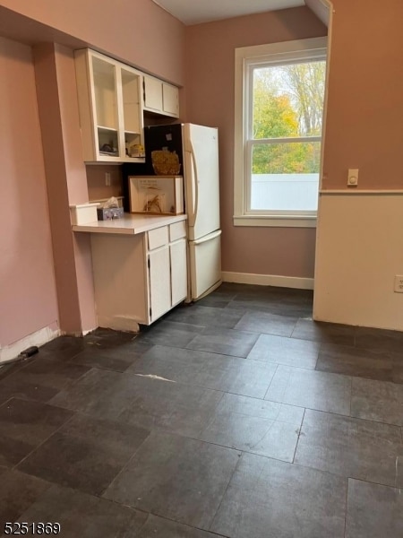 kitchen with white refrigerator, dark tile floors, and white cabinetry