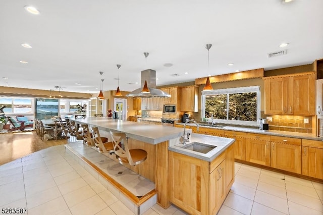 kitchen featuring a breakfast bar area, island range hood, sink, a kitchen island with sink, and light tile patterned flooring