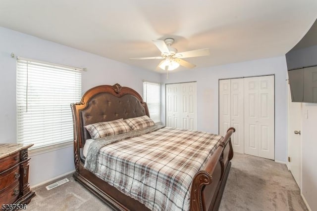 bedroom featuring light carpet, baseboards, a ceiling fan, and multiple closets