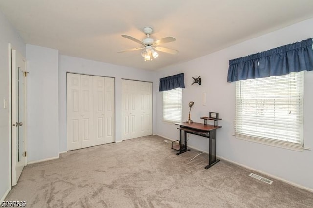 interior space with light carpet, baseboards, visible vents, ceiling fan, and multiple closets