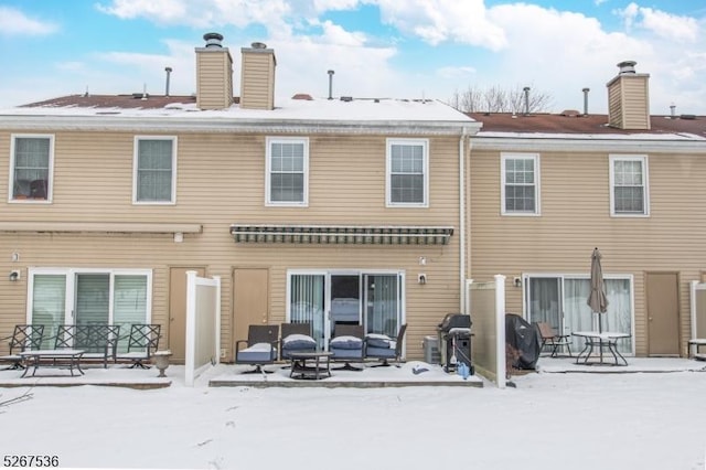 snow covered back of property with a patio area and a chimney