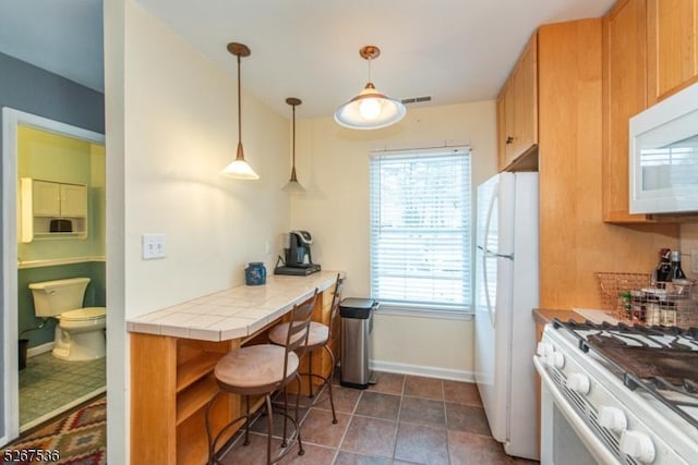 kitchen with pendant lighting, tile counters, visible vents, white appliances, and baseboards