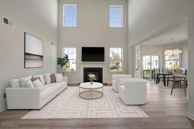 living room with an inviting chandelier, a wealth of natural light, light wood-type flooring, and a high ceiling