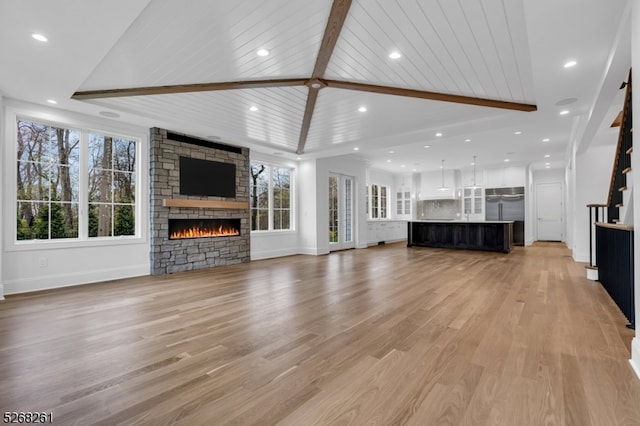 unfurnished living room with high vaulted ceiling, beam ceiling, light wood-type flooring, and a stone fireplace