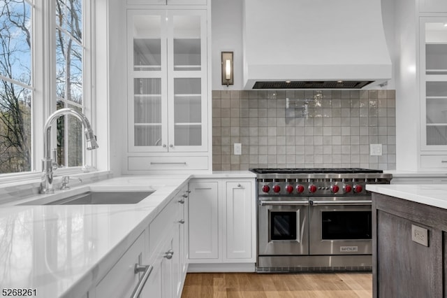 kitchen featuring premium range hood, double oven range, tasteful backsplash, white cabinets, and light wood-type flooring