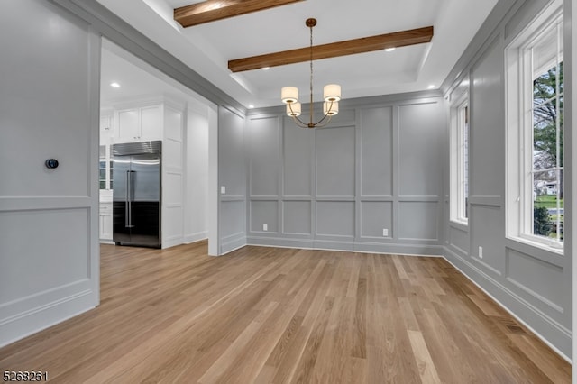 unfurnished room with a healthy amount of sunlight, beam ceiling, and light wood-type flooring