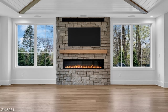 unfurnished living room with hardwood / wood-style flooring, a healthy amount of sunlight, and a stone fireplace