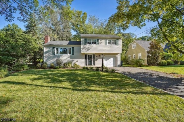 split level home featuring an attached garage, driveway, a chimney, and a front yard