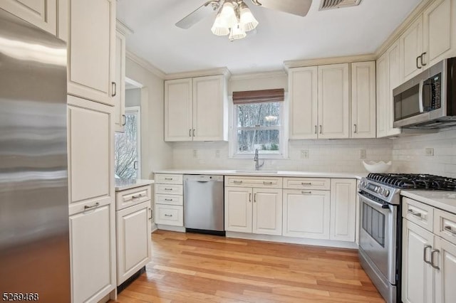 kitchen with stainless steel appliances, tasteful backsplash, light countertops, light wood-style flooring, and a sink