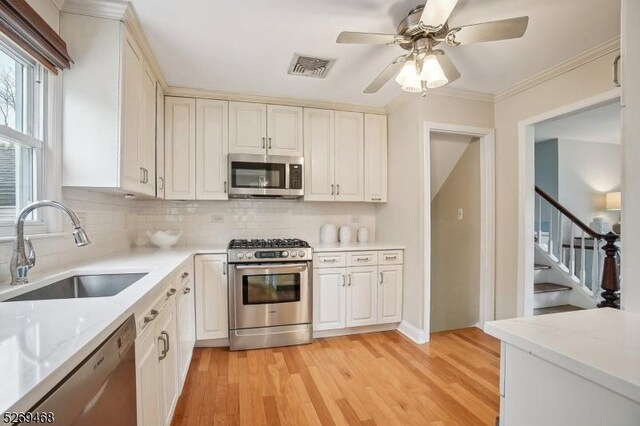 kitchen with stainless steel appliances, visible vents, backsplash, a sink, and light wood-type flooring