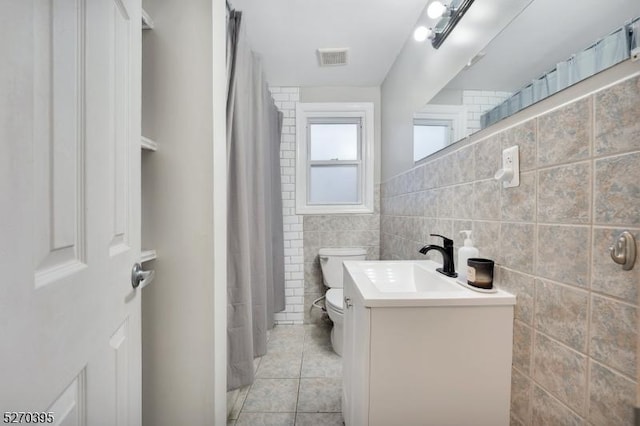 bathroom featuring toilet, vanity, tile patterned floors, and tile walls