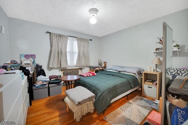 bedroom with a textured ceiling, light wood-type flooring, and radiator