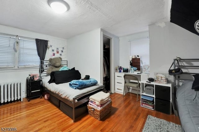 bedroom with radiator heating unit, wood-type flooring, and a textured ceiling