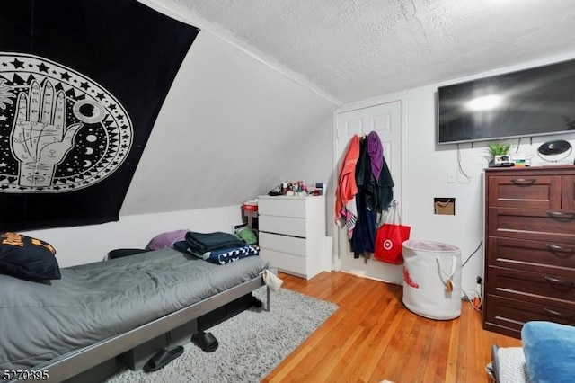 bedroom featuring light hardwood / wood-style floors, a textured ceiling, and vaulted ceiling