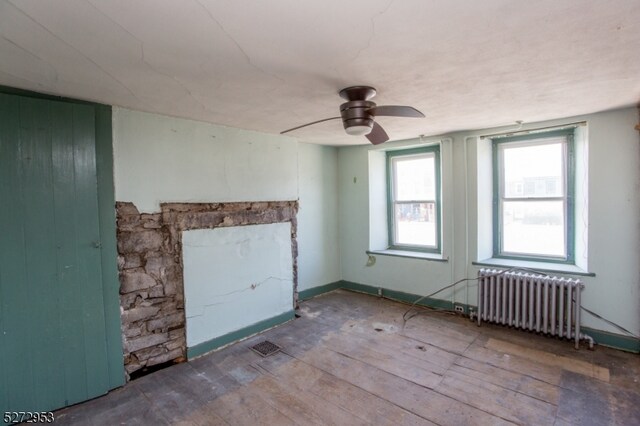 empty room with a fireplace, ceiling fan, radiator heating unit, and hardwood / wood-style flooring
