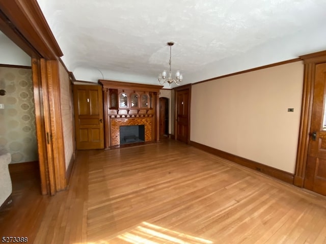 unfurnished living room with ornamental molding, a notable chandelier, and light hardwood / wood-style flooring