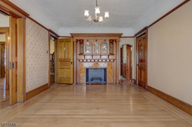 unfurnished living room with crown molding, a tile fireplace, a chandelier, and light hardwood / wood-style floors