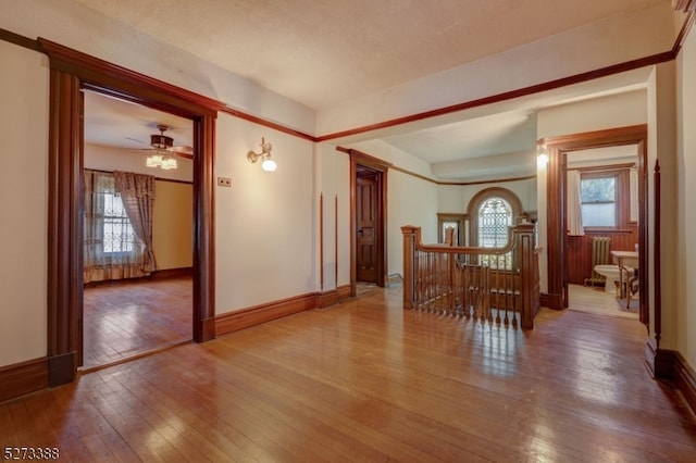 empty room with ceiling fan, radiator, hardwood / wood-style floors, and a healthy amount of sunlight