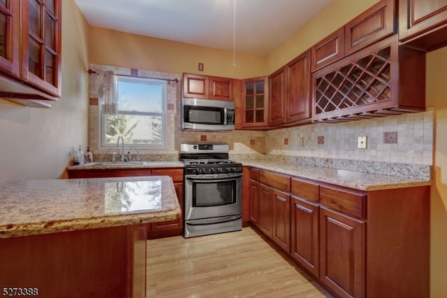 kitchen featuring appliances with stainless steel finishes, light wood-type flooring, tasteful backsplash, sink, and light stone countertops