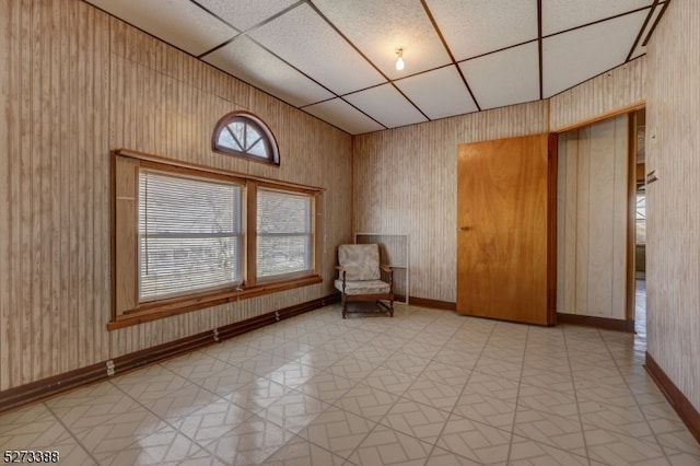 unfurnished room featuring light tile flooring, wooden walls, and a drop ceiling