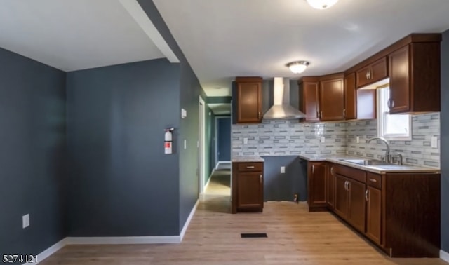 kitchen featuring wall chimney exhaust hood, sink, light hardwood / wood-style floors, and decorative backsplash