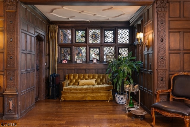 living area featuring ornamental molding, wooden walls, and dark hardwood / wood-style flooring