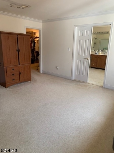 unfurnished bedroom featuring ornamental molding, connected bathroom, a spacious closet, a closet, and light tile floors